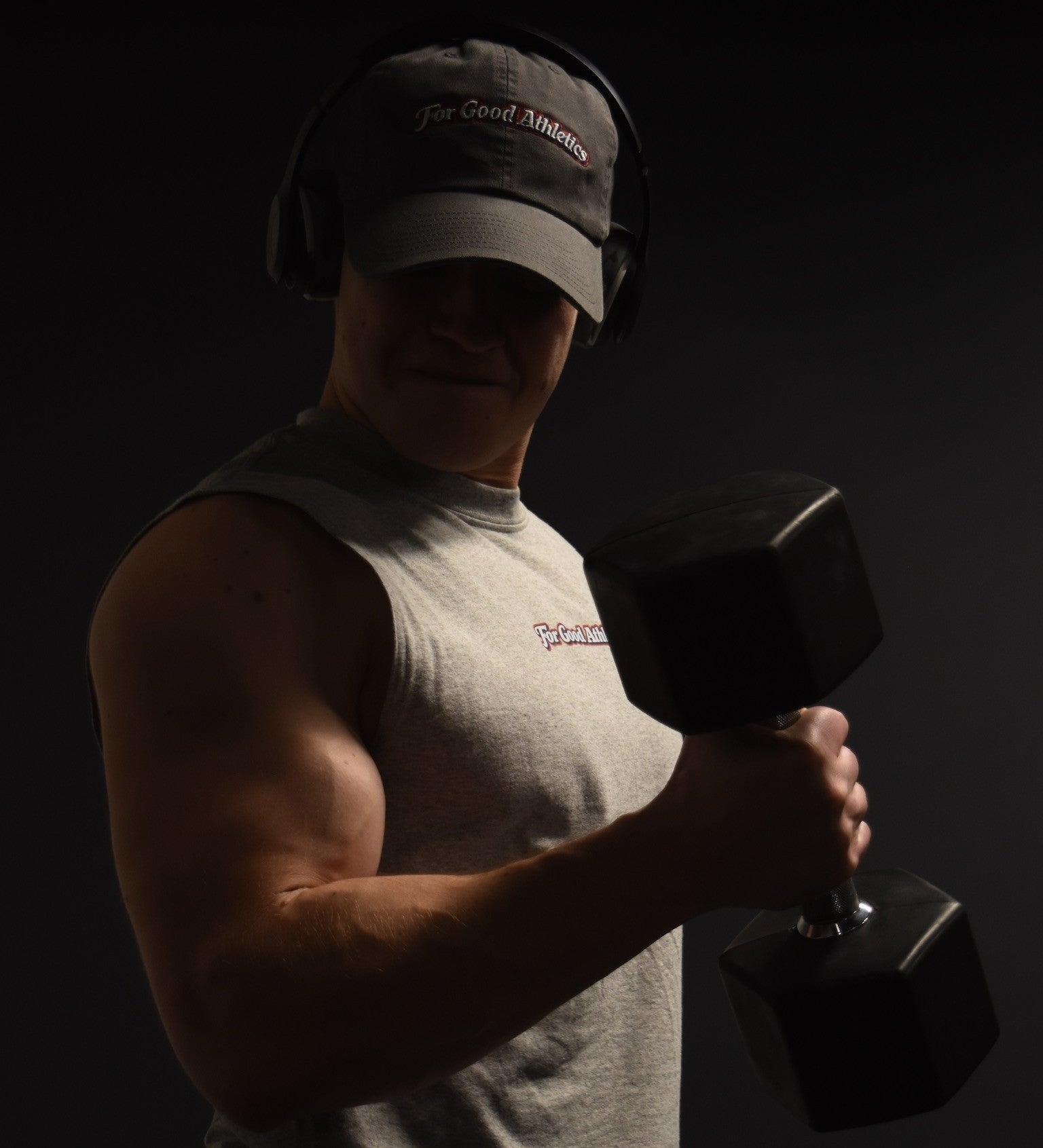 Man lifting a dumbbell with headphones on a dark background